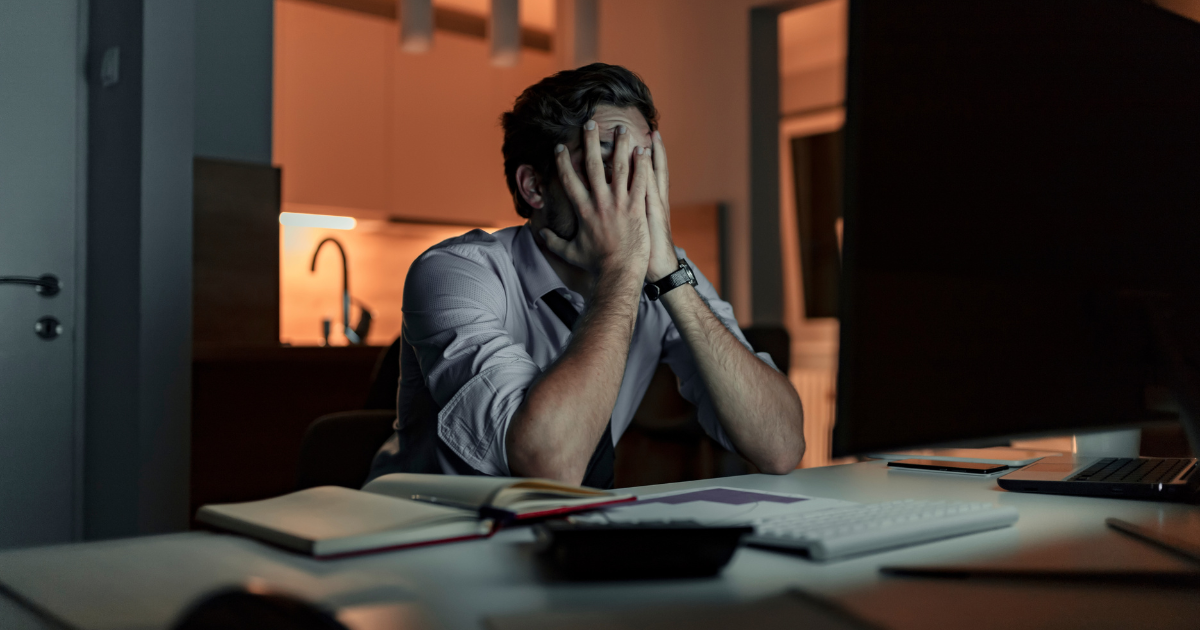 The image shows a man who is sitting on his desk burnt out because of job search